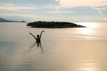 Obraz premium Silhouette shot of Asian women raise hand and enjoy vacation inside infinite pool with ocean sunset view and island at the background. Holiday lifestyle at tropical beach.
