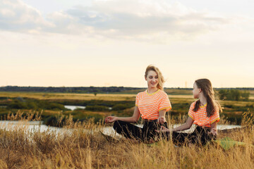 Fototapeta premium Young mother with her daughter in same clothes making yoga outdoors.