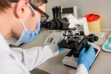 In the hospital laboratories working process, a young man doctor is looking in the medical microscope