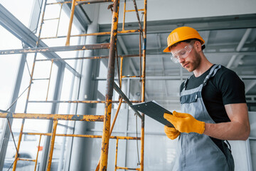 Engineer in grey uniform with notepad in hands works indoors in modern big office at daytime