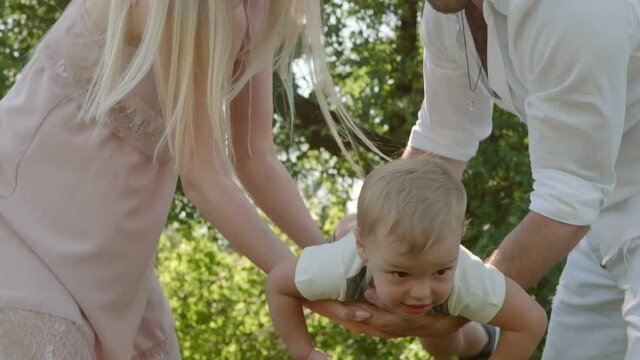 young parents rocking their little child in their arms. dad and mom spend time with their son. family together in prak