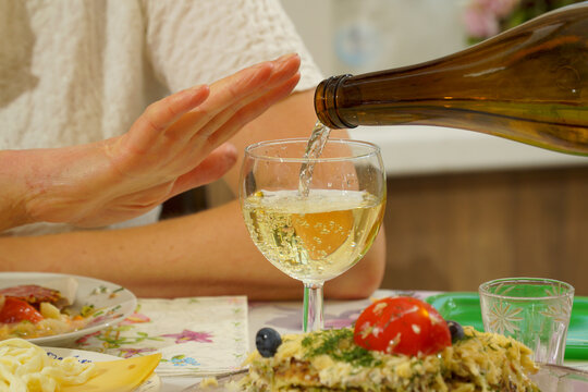 The hand of a young woman gestures that she has enough wine.