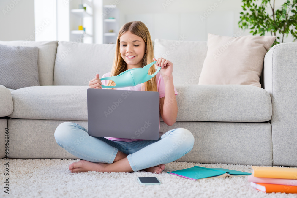 Sticker Full size photo of small pupil kid sit floor study remote use laptop have online meeting teacher wear medical mask legs crossed folded in house indoors