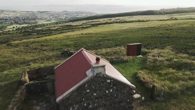 Aerial reveal of traditional stone cottage in Irish countryside with ocean views