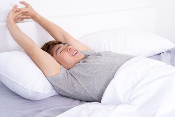 Young Asian man stretching in bed after wake up from the good comfortable bed. Healthcare medical or daily life concept.