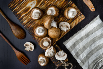 Fototapeta na wymiar Brown champignon with cutting board on a kitchen table. Dark background. Top view