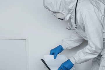 Male doctor scientist in lab coat, defensive eyewear and mask holding notepad in hands