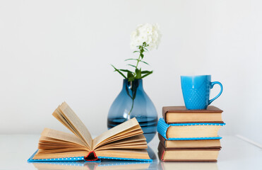 Cozy home interior decor: stack of books, cup of coffee and vase with white flower on a glass...