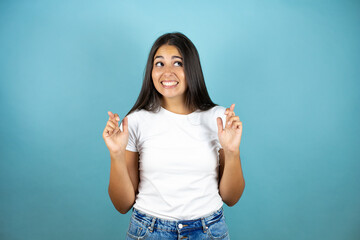 Fototapeta premium Young beautiful woman over isolated blue background gesturing finger crossed smiling with hope and looking side