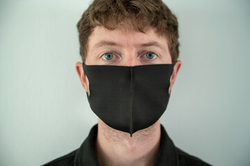 Man with black medical mask on face. Front profile portrait of man looking deeply into the lens. Safety precautions to help through this global pandemic. Health care & medical concept.