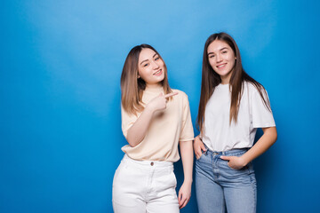 Portrait of multinational joyful women in casual clothes smiling and pointing to each other isolated over blue background