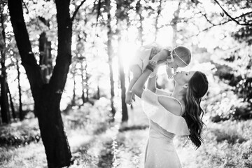 Beautiful woman with baby girl walking at the park, lovely mother kissing adorable daughter, caring parent lifts in air cute toddler, enjoy happy family moments, weekend outdoors, parenthood concept