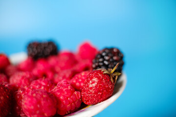 raspberries, strawberry and blackberry on a plate blue background