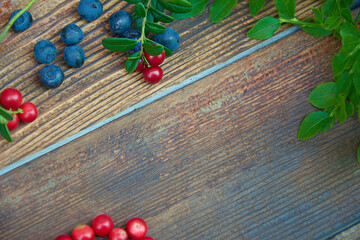 Wild berry on dark rustic wooden background. Cranberries and blueberries with green leaves on old wooden table with copyspace. Top view. Selective focus.