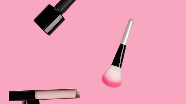 Different makeup accessories fly on trendy pastel pink background. Beauty animation. Cosmetic products. Make-up tools set concept. Lipstick, mascara, brush, perfume, nail Polish fall down. Skin care.