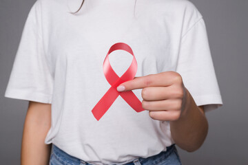 Woman holding breast with pink ribbon over white background. Concept photo to support breast cancer cause. - Powered by Adobe