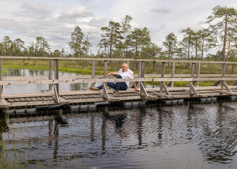 the summer swamp. a man in a white shirt sits on a wooden bridge. bog pond. bog background and vegetation