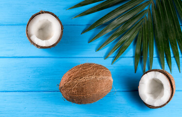 Coconuts whole and halved. With palm leaves on a blue background. View from above.
