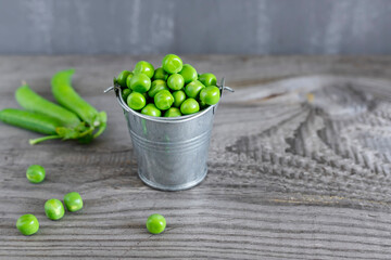 Close-up view of fresh green peas in a small metal bucket on dark wooden table.