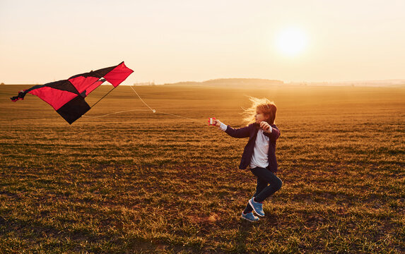 Happy little girl running with kite in hands on the beautiful field at sunrishe time