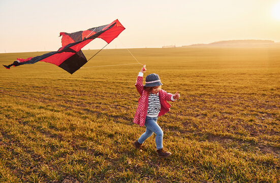 Happy little girl running with kite in hands on the beautiful field at sunrishe time