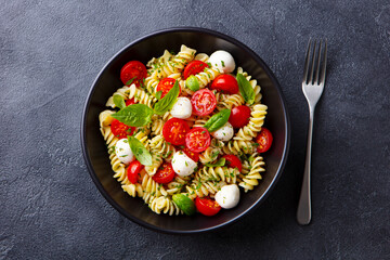Pasta fusilli with mozzarella cheese, tomatoes and basil. Dark background. Close up. Top view.