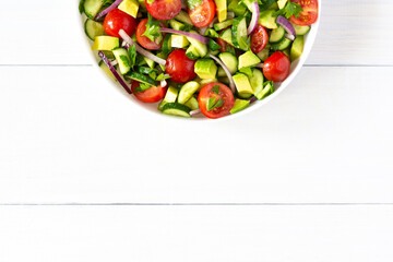Salad of fresh ripe tomato, onion, avocado, cucumber and parsley and olive oil, salad in a white plate on white wooden background