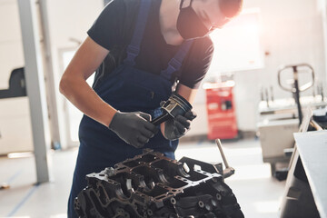 Professional repairman in black protective mask works with broken automobile engine