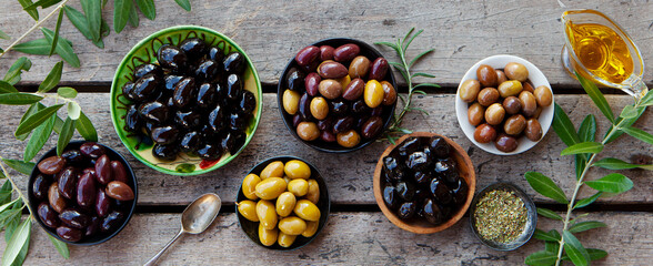 Assortment of fresh olives on a plate with olive tree brunches. Wooden background. Top view.