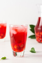 Summer delicious refreshing compote of cherries with pulp and with ice in glasses on a white background, a jug with a drink