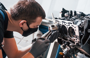 Professional repairman in black protective mask works with broken automobile engine