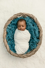 sleepy swaddled African-American newborn baby boy laying on a blue rug in a basket with copy space