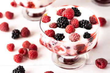Delicious juicy berries of raspberries and blackberries with yoghurt in a glass form on a white background