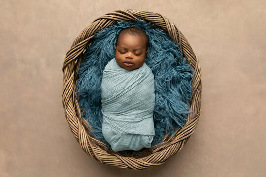sleepy swaddled African-American newborn baby boy laying on a blue rug in a basket with copy space