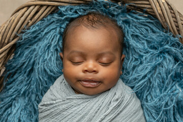 sleepy swaddled African-American newborn baby boy laying on a blue rug in a basket with copy space