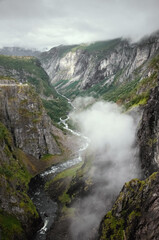 A gorge above a mountain river in Norway with a low floating cloud. View from above.