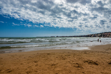 Nettuno, Lazio, Rome, Italy - Some people bathe, play and relax in the water, in the Roman sea. Reflections of light on the water. Cloudy blue sky at sunset in summer. Waves of the sea slightly choppy