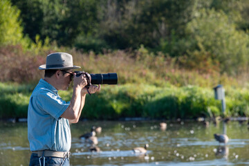 望遠レンズ付けた一眼レフカメラで野鳥撮影をするサングラスをかけたアジア人男性　　バンクーバー　ブリティッシュコロンビア　カナダ
