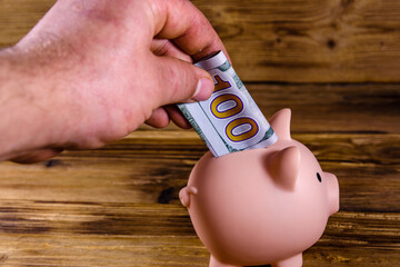 Man putting one hundred dollar bill in the pink piggy bank