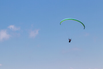 Naklejka na ściany i meble Paraglider gliding on blue sky with yellow parachute. 