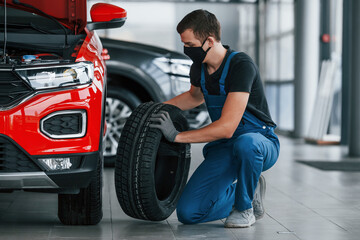 Obraz na płótnie Canvas Man in uniform changing tire of automobile. Conception of car service