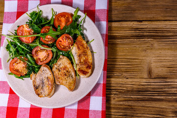Roasted chicken breasts and salad with arugula and cherry tomatoes in a ceramic plate. Top view