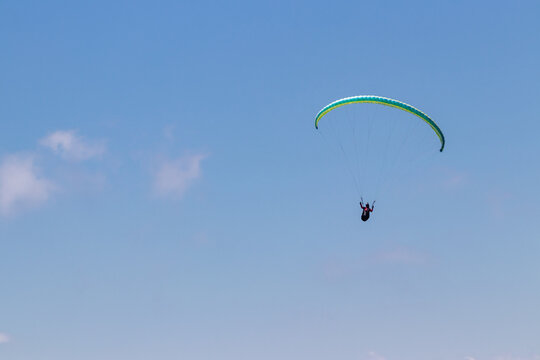 Paraglider gliding on blue sky with yellow parachute. 