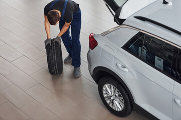 Top view of worker in black and blue uniform that is with car wheel working indoors