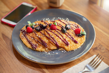 Hot cake breakfast set with red berries on a wooden table with a cell phone on one side. Breakfast concept in the morning with natural light.