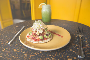 Tuna mexican toast with avocado and germ in yellow plate with glass of green juice on design table. Healthy food concept. Mexican healthy food.
