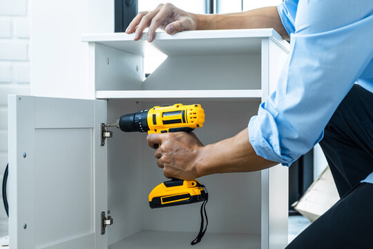 Man doing renovation work at home drilling wood with drill tack on locker