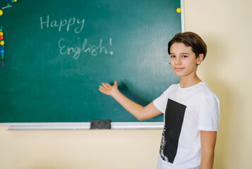 Schoolboy showing notes at blackboard in school. English lesson. Boy working in class.