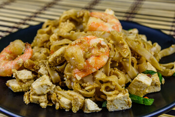Black plate with pad thai on a bamboo mat