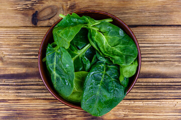 Ceramic bowl with spinach leaves on rustic wooden table. Top view